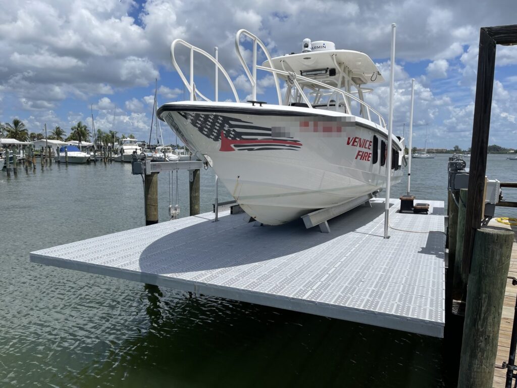 A center console rescue boat raised on a full deck aluminum elevator boat lift with grate platform panels and a piling mounted lift motor. Boat lift installation by Anderson Dock and Lift, Sarasota County FL.