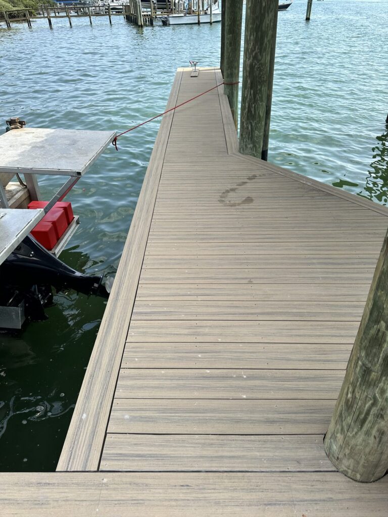 A composite decked dock walkway runs over green water on wood pilings to a lower platform, with an aluminum lift frame and a boat with an outboard motor alongside. Dock and boat lift work by Anderson Dock and Lift, Longboat Key FL.