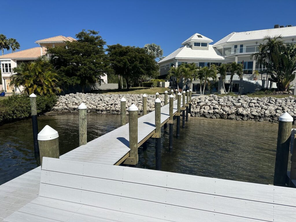 Gray composite dock walkway on capped pilings running in to a rock rip rap shoreline. Dock construction by Anderson Dock and Lift, Sarasota FL.