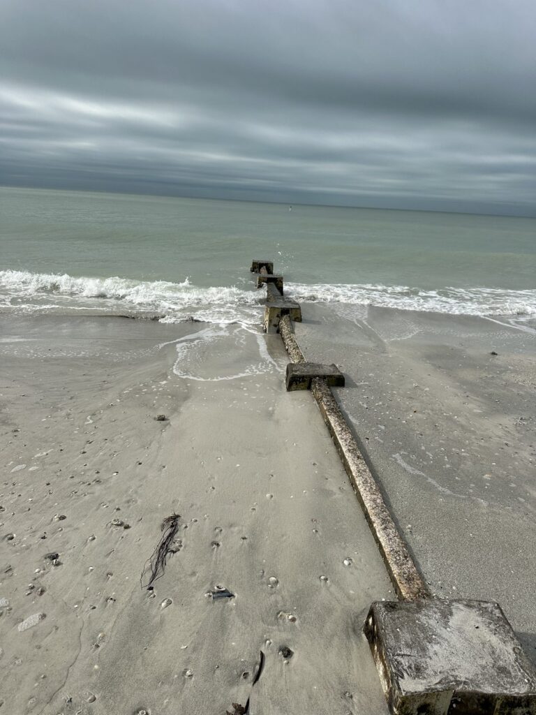 A low concrete groin with square post caps runs from the sand into the Gulf as waves wash along its edge. Shoreline and seawall work by Anderson Dock and Lift, Sarasota FL.