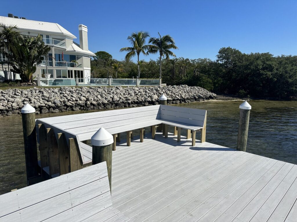 Bench with a backrest built into a gray composite dock platform above a rock rip rap shoreline. Custom dock construction by Anderson Dock and Lift, Sarasota FL.