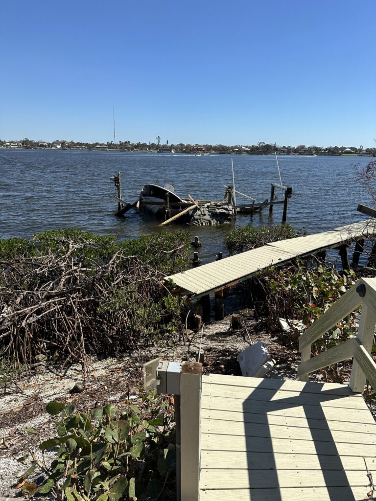 A gray board dock walkway with a wood railing crosses mangroves and a shell shoreline toward open bay water. Dock and pier construction by Anderson Dock and Lift, Bradenton FL.