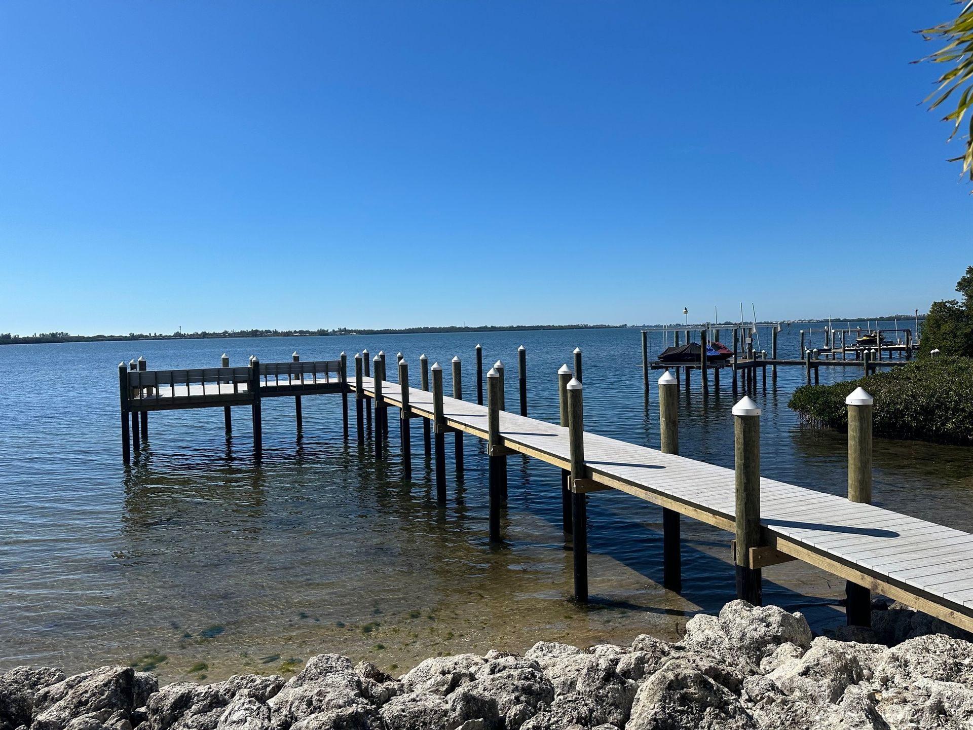 Composite pier with a railed platform extending over clear bay water past a riprap shoreline. Custom pier construction, Anderson Dock and Lift, Anna Maria Island FL.