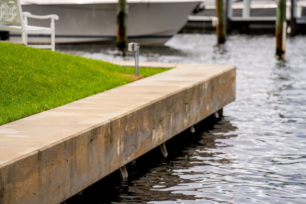 Concrete cap on a waterfront retaining wall beside a lawn at a marina. Retaining wall installation and repair, Anderson Dock and Lift, Bradenton FL.