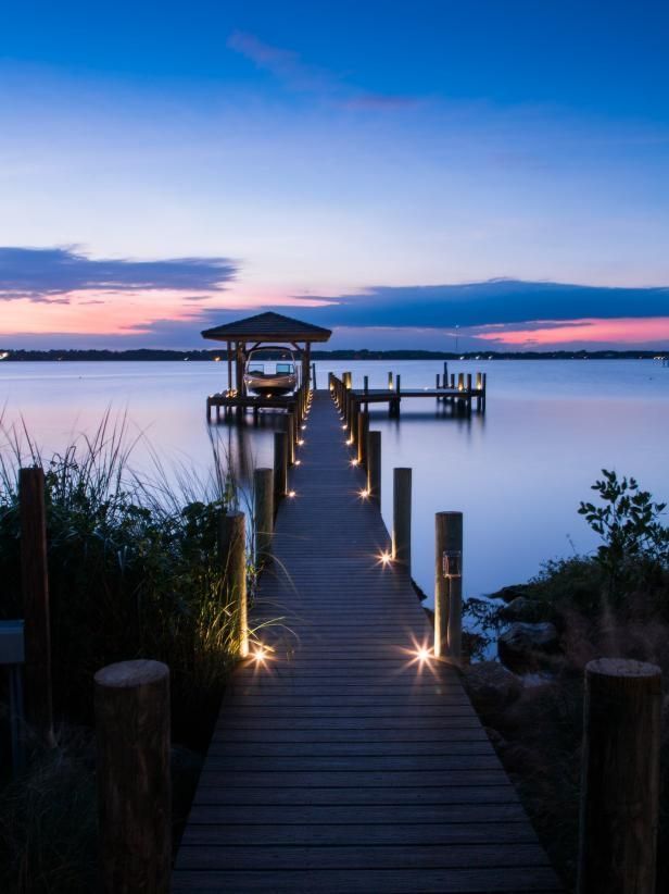 Wooden pier extends over calm water at dusk, illuminated by lights, leading to a gazebo. Pier construction by Anderson Dock and Lift, Palmetto FL.