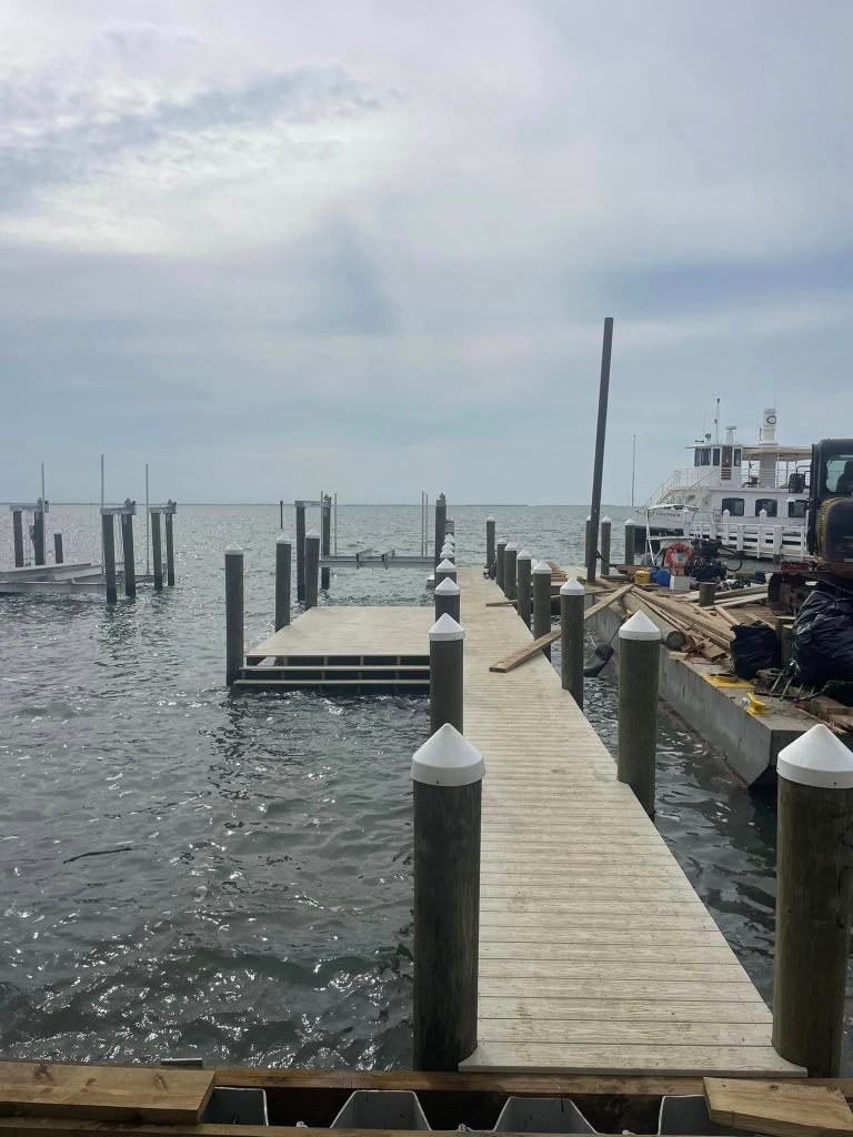 Wooden pier with pilings extends into open water with a boat docked nearby. Pier construction by Anderson Dock and Lift, Palmetto FL.