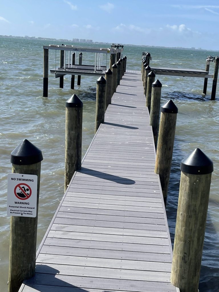 Long dock walkway with black capped pilings leading to a boat lift platform. Dock and boat lift construction by Anderson Dock and Lift, Cortez FL.