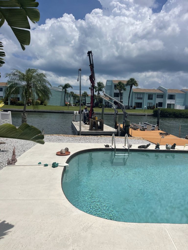 Crane setting dock materials beside a pool during construction. Dock builder Anderson Dock and Lift, Apollo Beach FL.