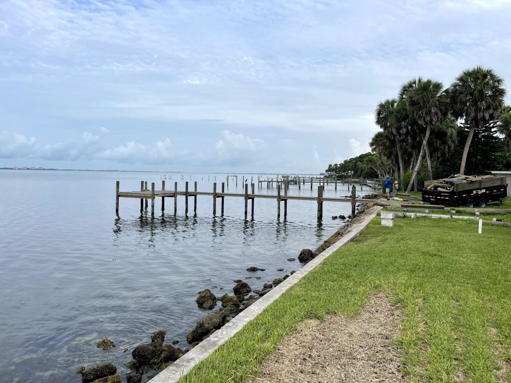 Long residential dock over calm water with a seawall and rock rip rap along the lawn. Dock and seawall construction by Anderson Dock and Lift, Bradenton FL.
