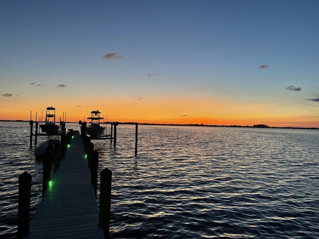 Dock at sunset with two boats moored and green LED deck lighting. Custom dock construction by Anderson Dock and Lift, Sarasota FL.