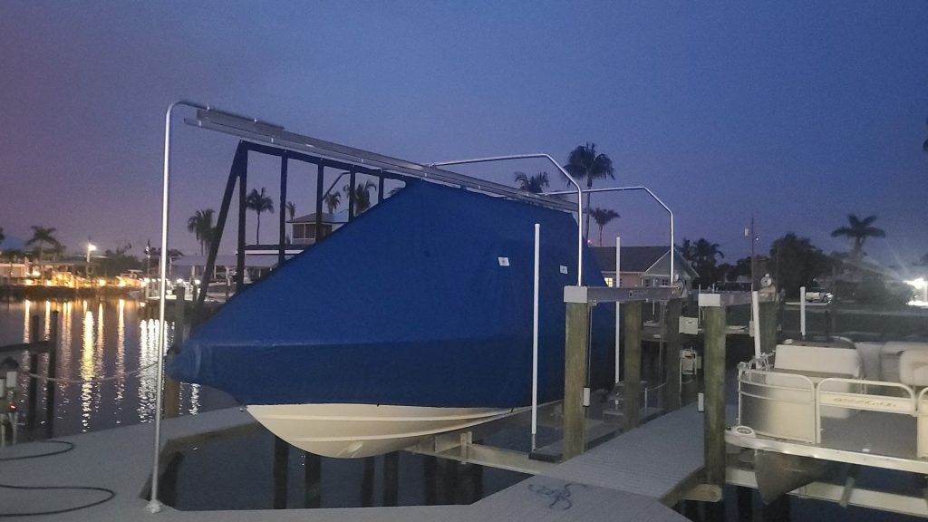 Covered boat resting on a boat lift at dusk with dock lighting on the water. Boat lift installation, Anderson Dock and Lift, Sarasota FL.