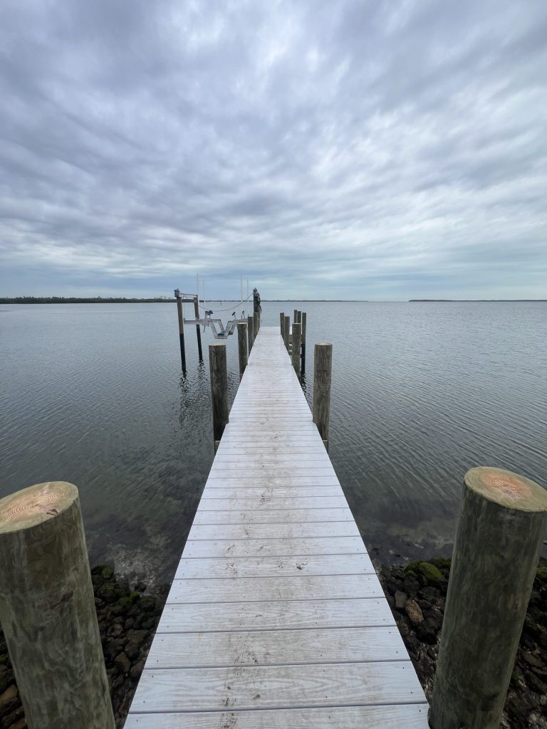 Dock with capped pilings running out over a rock rip rap shoreline. Dock builder Anderson Dock and Lift, Fort Myers FL.