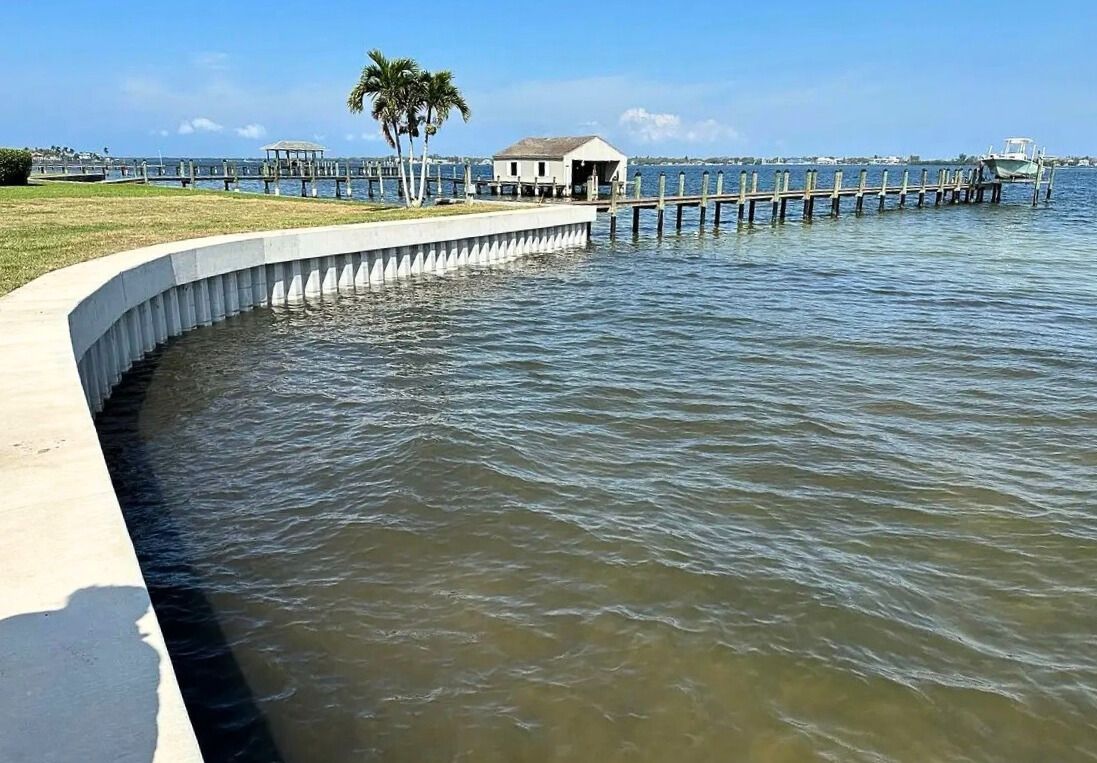 Curved concrete seawall with a new cap along a bayfront lawn and fishing pier. Seawall construction, Anderson Dock and Lift, Manatee County FL.